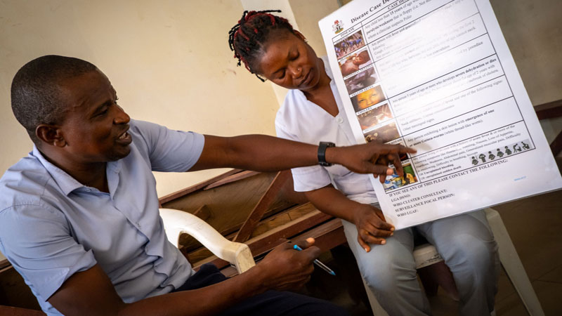 Health communications Nigeria - Male Doctor point to a large health poster held by a female nurse